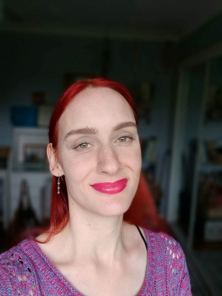 Suzanna wearing purple knit shirt and smiling with pink lipstick on