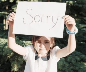 young girl holds up a sign apologising for our autistic children