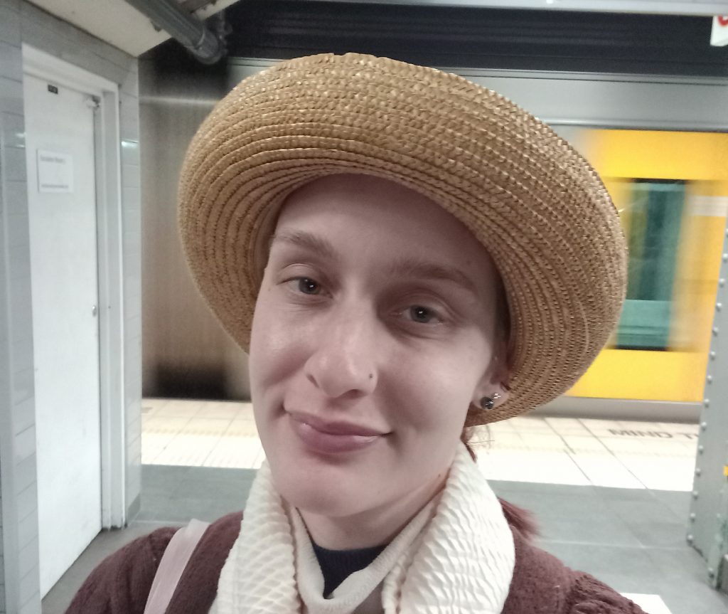 A List Socialite Suzanna smiling wearing a straw hat and a scarf with a train speeding past in the background