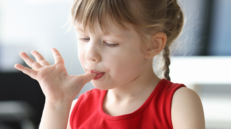 A young autistic girl is licking her fingers